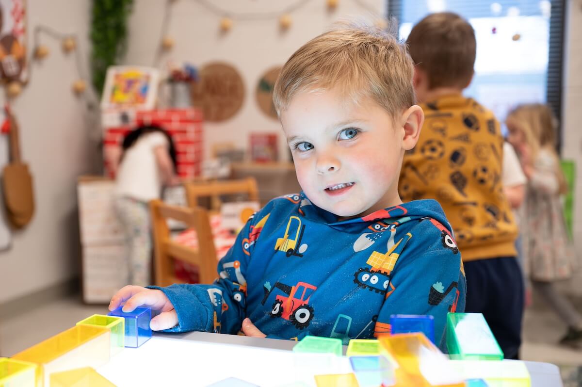 DT_Interior_Light Table Preschool boy in a blue hoodie decorated with trucks, playing with translucent building blocks at a light table.