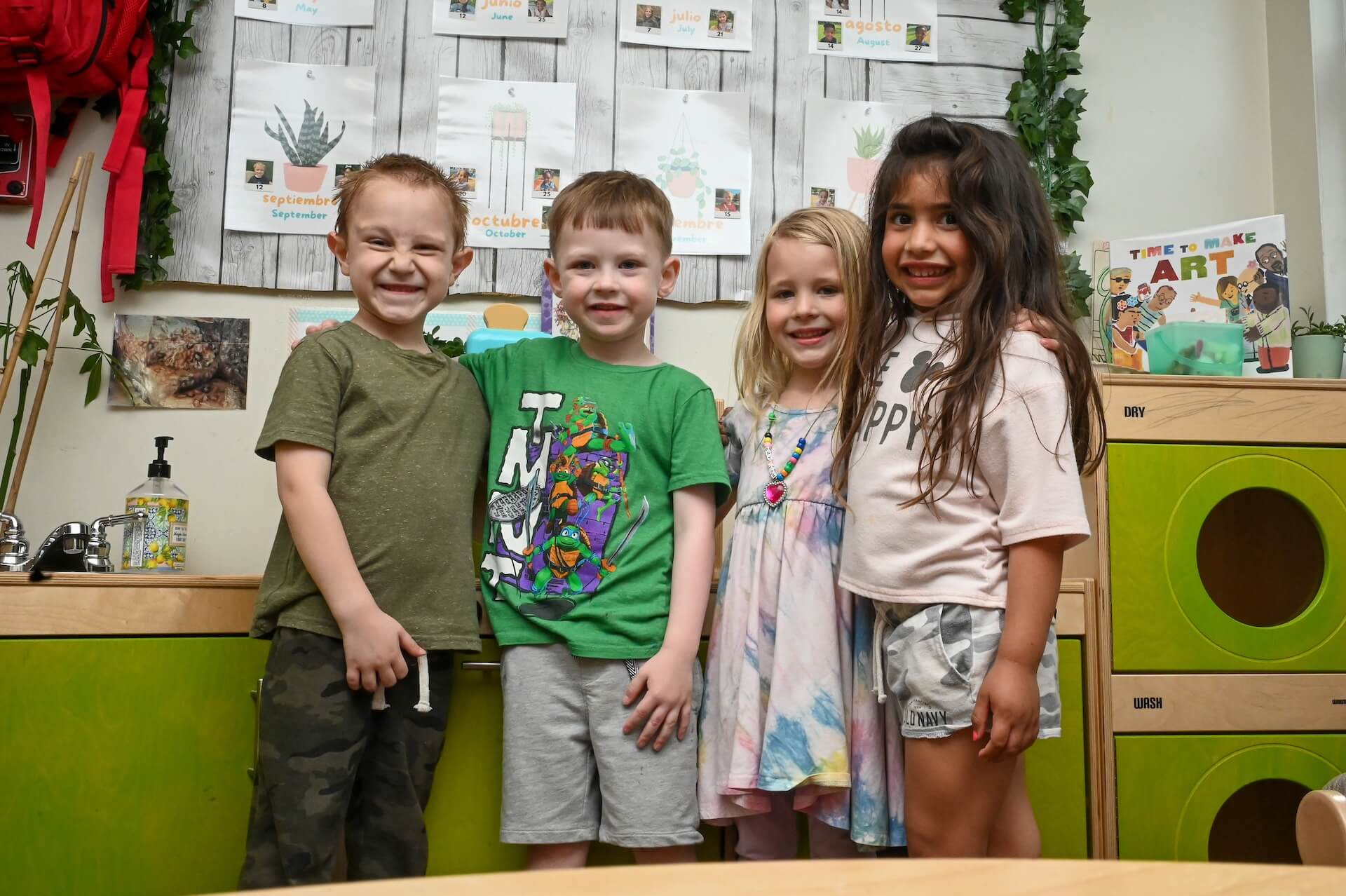 PreK_2 Group of four smiling preschool children standing together in the classroom for a group photo.