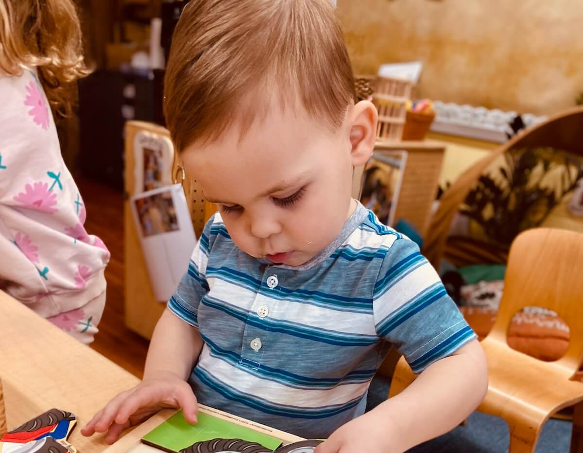 Puzzle Toddler concentrating on completing a wooden animal puzzle at a classroom table.