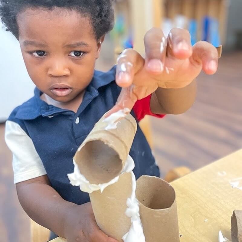Threes_5 Focused preschool boy gluing cardboard tubes together during a creative building activity