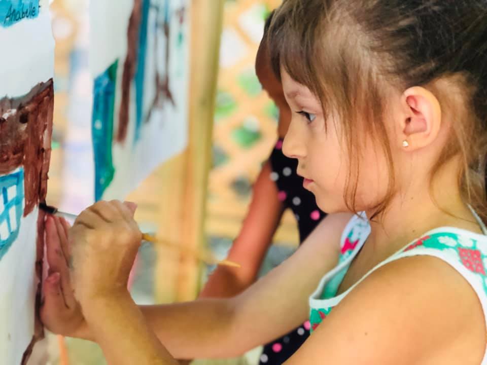PV Young girl in a classroom focusing on threading a string through a number card during a hands-on learning activity.