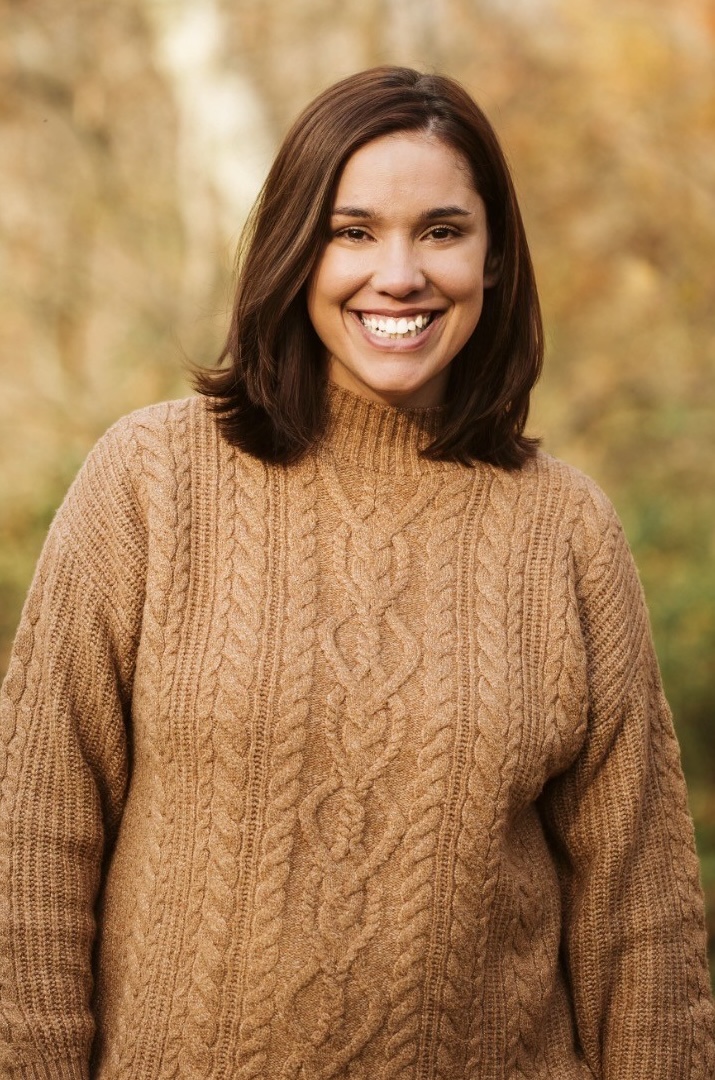 Professional headshot of Jeanine Ali smiling, wearing a white shirt and black sweater vest.